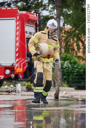 Firefighter Carrying Rolled Fire Hose Near Red Fire Truck During Wet Emergency Response Training Firefighter Carrying Rolled Fire Hose Near Red Fire Truck During Wet Emergency Response Training 143012794