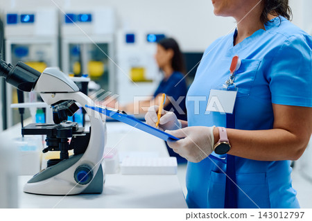 Lab technician examining samples and recording data in a modern laboratory setting during daytime Lab technician examining samples and recording data in a modern laboratory setting during daytime 143012797