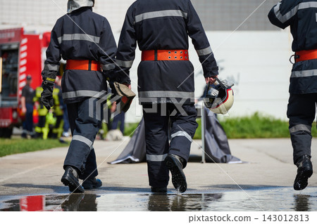 Firefighters Walking to Emergency Scene in Turnout Gear With Helmet and Fire Truck Nearby Firefighters Walking to Emergency Scene in Turnout Gear With Helmet and Fire Truck Nearby 143012813
