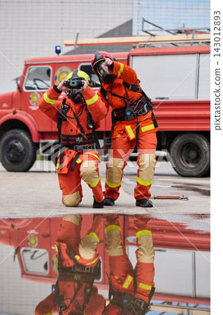 Firefighters in Orange Protective Gear Survey Scene and Point Near Red Fire Truck During Training Firefighters in Orange Protective Gear Survey Scene and Point Near Red Fire Truck During Training 143012893