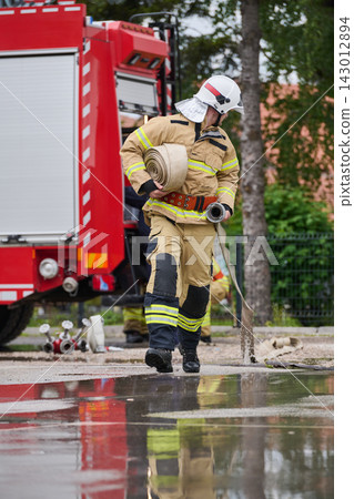 Firefighter Carrying Hose Next To Red Fire Truck During Emergency Response Training Exercise Firefighter Carrying Hose Next To Red Fire Truck During Emergency Response Training Exercise 143012894