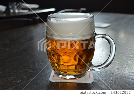 Single beer mug with creamy foam on dark wooden table in prague tavern for menu photo and beverage advertising background Single beer mug with creamy foam on dark wooden table in prague tavern for menu photo and beverage advertising background 143012932