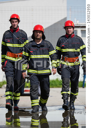 Three Firefighters Walking Confidently in Protective Uniforms With Red Helmets and Reflective Stripes Three Firefighters Walking Confidently in Protective Uniforms With Red Helmets and Reflective Stripes 143012950