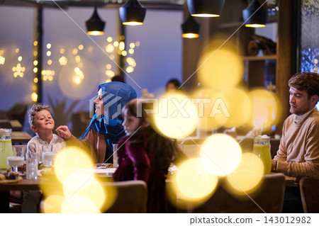 Family Dinner in a Festive Restaurant With Mother Wearing Hijab and Children Enjoying Evening Family Dinner in a Festive Restaurant With Mother Wearing Hijab and Children Enjoying Evening 143012982
