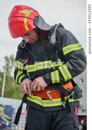 Firefighter Buckling Safety Harness and Wearing Red Helmet With Reflective Stripes During Rescue Preparation Firefighter Buckling Safety Harness and Wearing Red Helmet With Reflective Stripes During Rescue Preparation 143012983