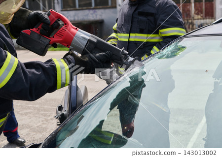 Firefighters Performing Vehicle Extrication Cutting Windshield During Emergency Car Rescue Operation 143013002