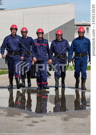 Firefighters Team Walking Together in Uniform With Red Helmets and Reflective Puddle Reflection Firefighters Team Walking Together in Uniform With Red Helmets and Reflective Puddle Reflection 143013030