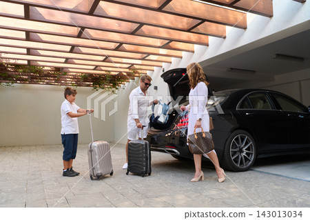 Family Packing Luggage Into Luxury Black Car In Covered Garage Preparing For Vacation Departure Family Packing Luggage Into Luxury Black Car In Covered Garage Preparing For Vacation Departure 143013034