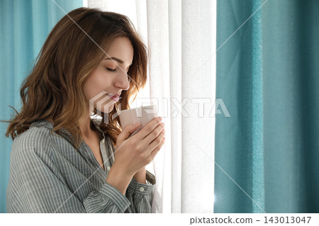 Woman drinking coffee near window with beautiful curtains at home 143013047