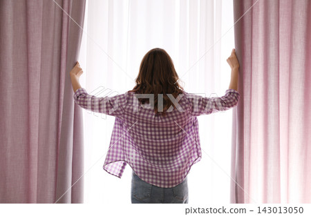 Woman opening window curtains at home in morning, back view Woman opening window curtains at home in morning, back view 143013050