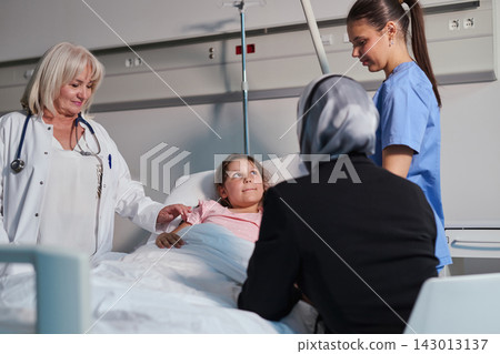 Nurse and doctor caring for young girl in hospital room with family member present during a medical check-up Nurse and doctor caring for young girl in hospital room with family member present during a medical check-up 143013137