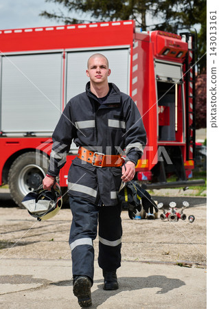 Firefighter In Protective Uniform Walking Toward Camera With Helmet And Fire Truck Behind 143013161