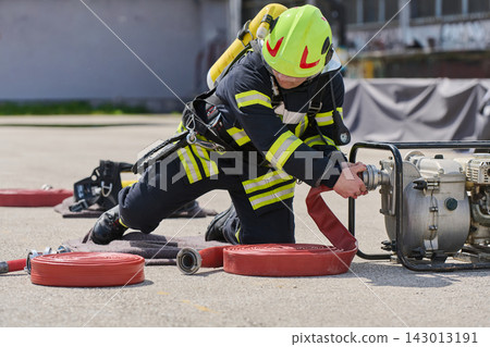 Firefighter Connecting Red Hose to Portable Pump During Emergency Training Exercise Outdoors Firefighter Connecting Red Hose to Portable Pump During Emergency Training Exercise Outdoors 143013191