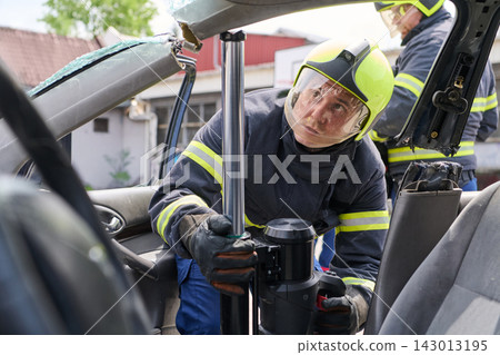 Firefighter Using Hydraulic Rescue Tool During Vehicle Extrication After Car Accident 143013195
