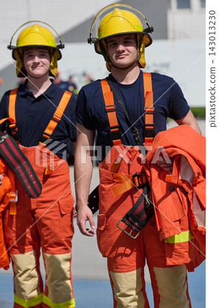 Young Firefighters in Yellow Helmets and Orange Protective Uniforms Standing Together During Training 143013230