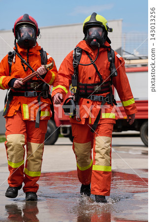 Two Firefighters In Orange Protective Gear Walking With Masks And Equipment Near Fire Truck Two Firefighters In Orange Protective Gear Walking With Masks And Equipment Near Fire Truck 143013256