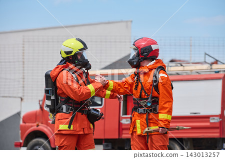Firefighters in Full Gear Shaking Hands Beside Red Fire Truck Showing Teamwork and Rescue Readiness 143013257