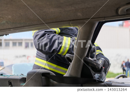 Firefighter Performing Vehicle Extrication With Hydraulic Tool During Car Accident Rescue Operation 143013264