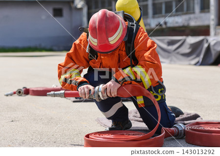 Firefighter Preparing Hose During Emergency Training Drill With Protective Gear and Breathing Apparatus Firefighter Preparing Hose During Emergency Training Drill With Protective Gear and Breathing Apparatus 143013292