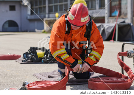 Firefighter Connecting Red Fire Hose During Emergency Training Drill Wearing Protective Gear Firefighter Connecting Red Fire Hose During Emergency Training Drill Wearing Protective Gear 143013310