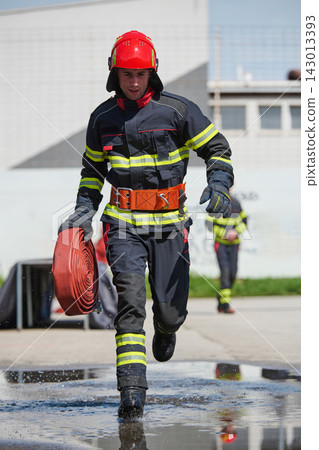 Firefighter Running With Hose In Protective Gear During Emergency Training Drill At Station Firefighter Running With Hose In Protective Gear During Emergency Training Drill At Station 143013393