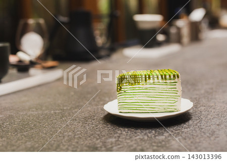 Slice of layered matcha green tea crepe cake served on a white plate in cafe. Slice of layered matcha green tea crepe cake served on a white plate in cafe. 143013396