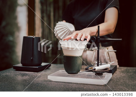 Barista placing a paper filter inside a ceramic coffee dripper on a cafe counter. Barista placing a paper filter inside a ceramic coffee dripper on a cafe counter. 143013398