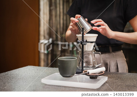 Barista pouring ground coffee beans into a ceramic dripper during brewing session. Barista pouring ground coffee beans into a ceramic dripper during brewing session. 143013399