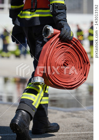 Firefighter Carrying Rolled Fire Hose In Safety Gear At Emergency Training Scene Firefighter Carrying Rolled Fire Hose In Safety Gear At Emergency Training Scene 143013592
