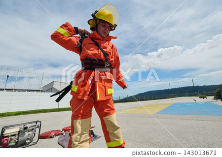 Firefighter In Orange Turnout Gear With Helmet Preparing Rescue Equipment On Helipad Firefighter In Orange Turnout Gear With Helmet Preparing Rescue Equipment On Helipad 143013671