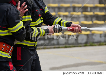 Firefighters Teamwork Using Hose to Spray Water During Outdoor Training Exercise at Stadium Firefighters Teamwork Using Hose to Spray Water During Outdoor Training Exercise at Stadium 143013689