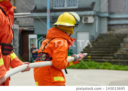 Firefighter Team Working With Hose During Outdoor Training Drill Wearing Orange Protective Gear And Helmet Firefighter Team Working With Hose During Outdoor Training Drill Wearing Orange Protective Gear And Helmet 143013695