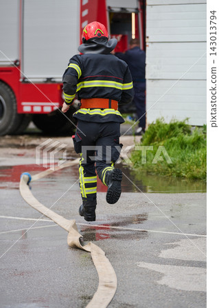 Firefighter Running With Hose Toward Fire Truck During Emergency Response Training Scene Firefighter Running With Hose Toward Fire Truck During Emergency Response Training Scene 143013794