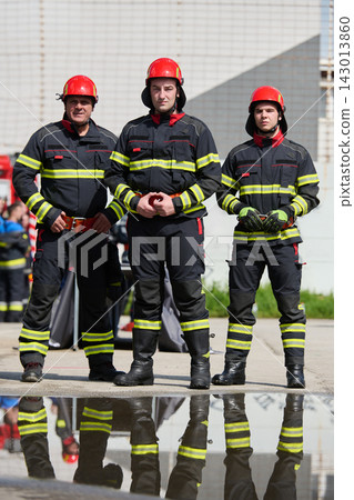 Three Firefighters Standing in Uniform With Helmets and Reflective Stripes Near Puddle Three Firefighters Standing in Uniform With Helmets and Reflective Stripes Near Puddle 143013860