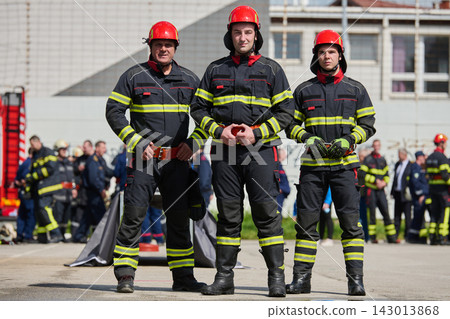 Three Firefighters Standing Together in Uniform With Red Helmets at a Rescue Drill Three Firefighters Standing Together in Uniform With Red Helmets at a Rescue Drill 143013868