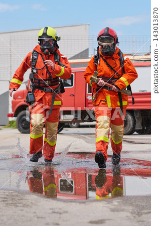 Firefighters In Protective Gear Running With Rescue Tools Beside A Red Fire Truck Firefighters In Protective Gear Running With Rescue Tools Beside A Red Fire Truck 143013870