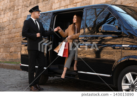 Professional driver helping woman with shopping bags to get out of car. Chauffeur service Professional driver helping woman with shopping bags to get out of car. Chauffeur service 143013890