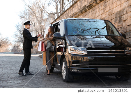 Professional driver helping woman with shopping bags to get out of car. Chauffeur service Professional driver helping woman with shopping bags to get out of car. Chauffeur service 143013891