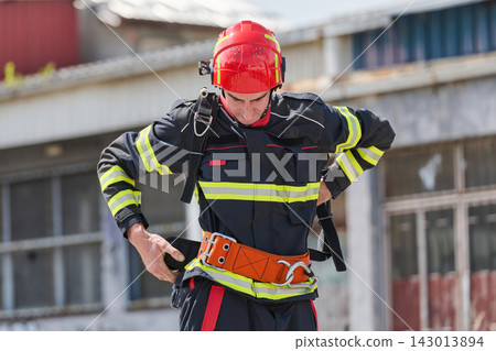 Firefighter Putting On Safety Harness and Red Helmet During Urban Rescue Training Drill Firefighter Putting On Safety Harness and Red Helmet During Urban Rescue Training Drill 143013894