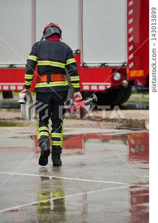 Firefighter Carrying Hose And Hydrant Toward Red Fire Truck On Wet Pavement During Emergency Response Firefighter Carrying Hose And Hydrant Toward Red Fire Truck On Wet Pavement During Emergency Response 143013899