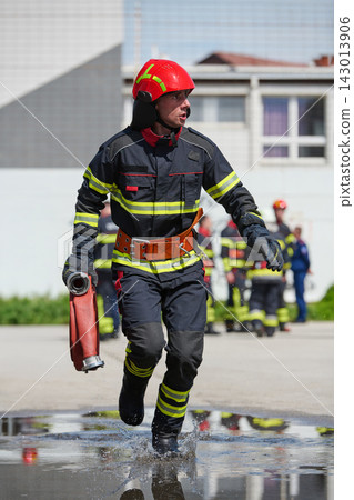 Firefighter Running With Hose During Emergency Training Drill In Protective Gear And Red Helmet Firefighter Running With Hose During Emergency Training Drill In Protective Gear And Red Helmet 143013906