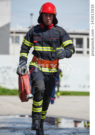 Firefighter Running With Hose In Protective Uniform And Helmet During Emergency Drill Firefighter Running With Hose In Protective Uniform And Helmet During Emergency Drill 143013916