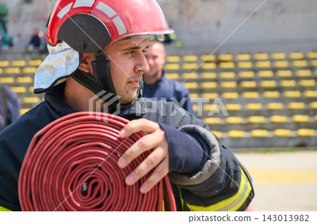 Firefighter Carrying Coiled Fire Hose Wearing Red Helmet And Protective Turnout Gear During Drill Firefighter Carrying Coiled Fire Hose Wearing Red Helmet And Protective Turnout Gear During Drill 143013982