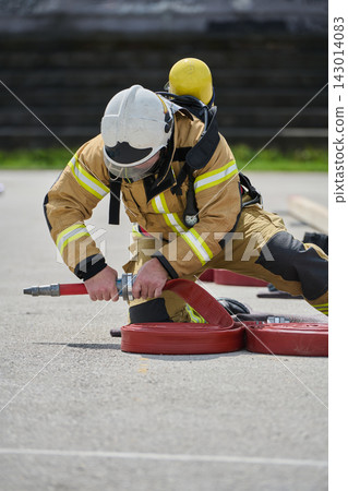 Firefighter Connecting Red Hose During Training Drill Wearing Full Protective Turnout Gear Firefighter Connecting Red Hose During Training Drill Wearing Full Protective Turnout Gear 143014083