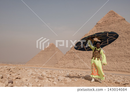 Proud Egyptian tanoura disc performer in lime green embroidered robe lifting a large decorated prop overhead against the ancient pyramids of Giza Proud Egyptian tanoura disc performer in lime green embroidered robe lifting a large decorated prop overhead against the ancient pyramids of Giza 143014084