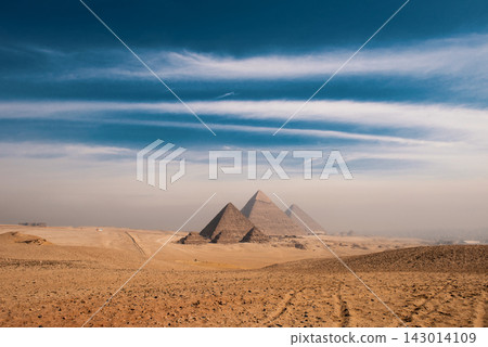 Ancient giza pyramids panoramic wide landscape across sandy desert plateau under dramatic two tone blue sky and hazy golden horizon Egypt travel Ancient giza pyramids panoramic wide landscape across sandy desert plateau under dramatic two tone blue sky and hazy golden horizon Egypt travel 143014109