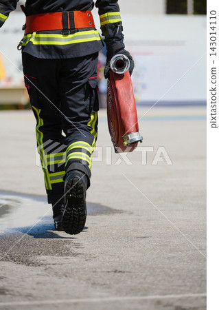 Firefighter Carrying Rolled Fire Hose in Protective Uniform Walking Away on Concrete Surface Firefighter Carrying Rolled Fire Hose in Protective Uniform Walking Away on Concrete Surface 143014110