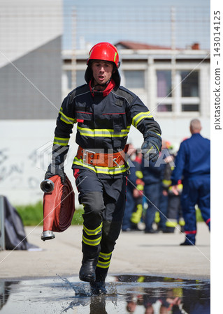Firefighter Running With Hose In Full Gear During Emergency Drill Or Rescue Response Firefighter Running With Hose In Full Gear During Emergency Drill Or Rescue Response 143014125