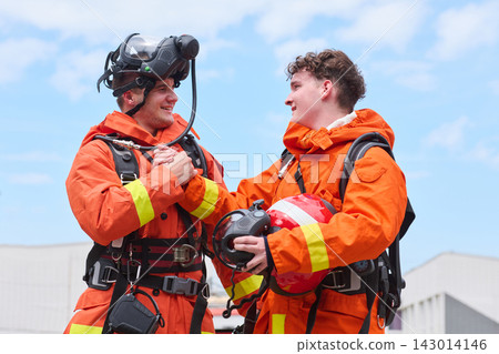 Two Firefighters in Orange Protective Gear Shaking Hands After Training With Helmets and Masks Two Firefighters in Orange Protective Gear Shaking Hands After Training With Helmets and Masks 143014146