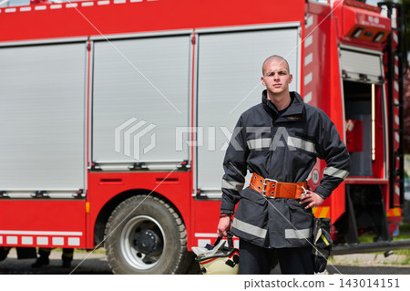 Young Firefighter Standing Confidently Next to Red Fire Truck Holding Helmet and Gear 143014151